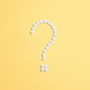 White pills arranged into a question mark shape on a vibrant yellow background.