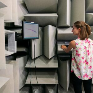 Female engineer testing sound waves in an anechoic chamber with a monitor.